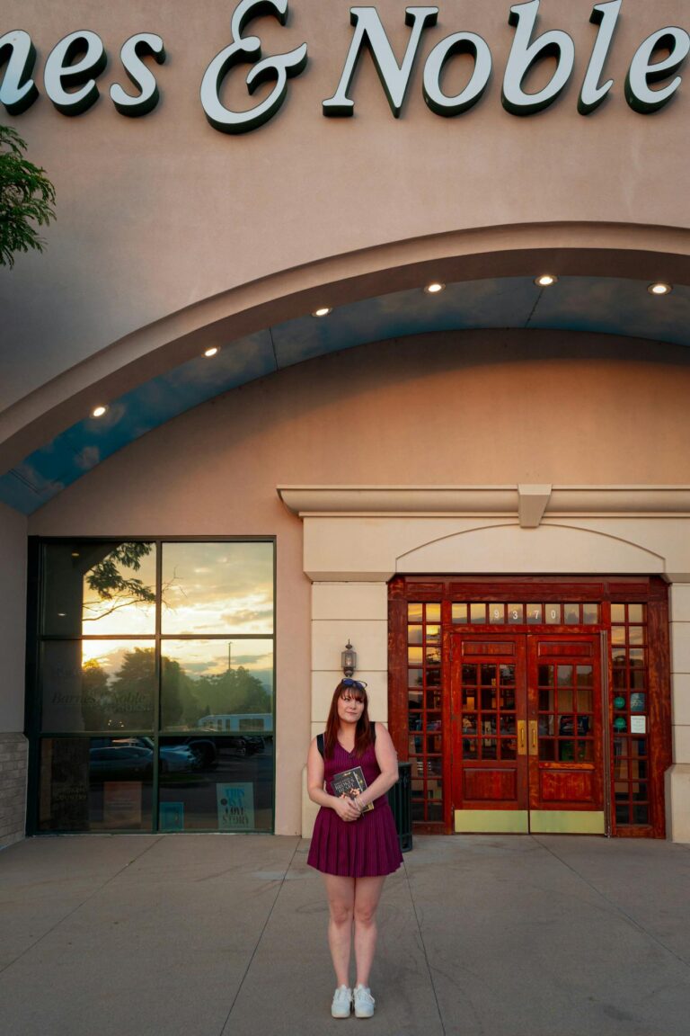 A young woman stands in front of Barnes & Noble, holding books at sunset in Westminster, Colorado.