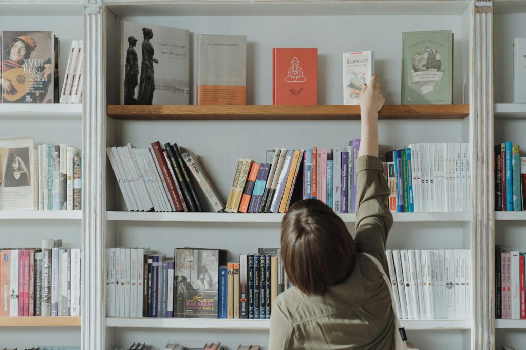 An individual browsing a bookshelf and reaching for a book in a bookstore setting.