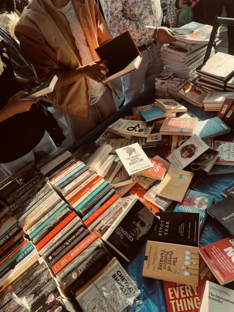 People browsing books at an outdoor market stall under warm lighting.